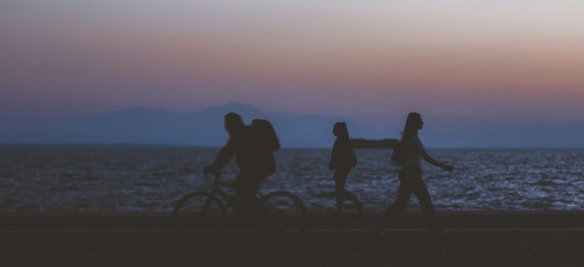creative unfocused humans wallpaper pattern of fuzzy walking people silhouettes on dark twilight waterfront along Pacific ocean and unfocused mountain horizon background in evening sunset time