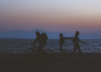 creative unfocused humans wallpaper pattern of fuzzy walking people silhouettes on dark twilight waterfront along Pacific ocean and unfocused mountain horizon background in evening sunset time